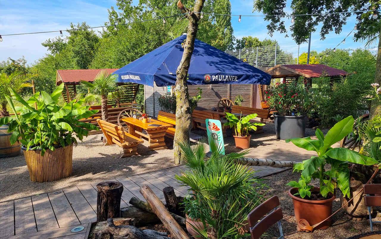 Biergarten der Schnitzel-Hütte mit Holzterrasse, Palmen und Paulaner-Sonnenschirm