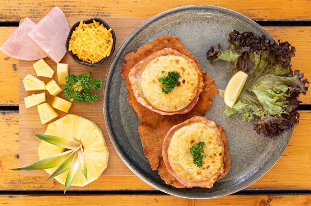 Zwei Schnitzel mit Ananas, Hinterschinken und geschmolzenem Cheddar überbacken