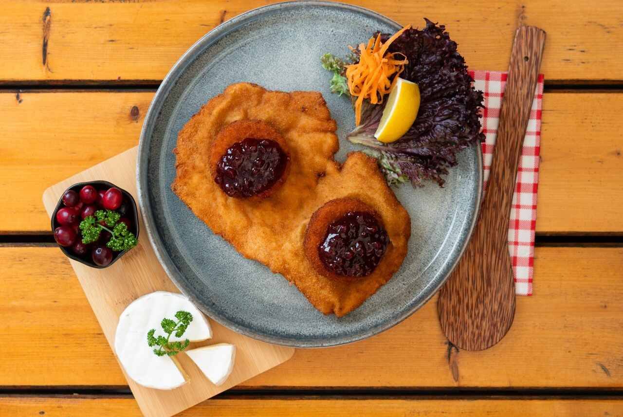 Halbes Schnitzel mit gebackenem Camembert und Preiselbeeren auf grauem Teller