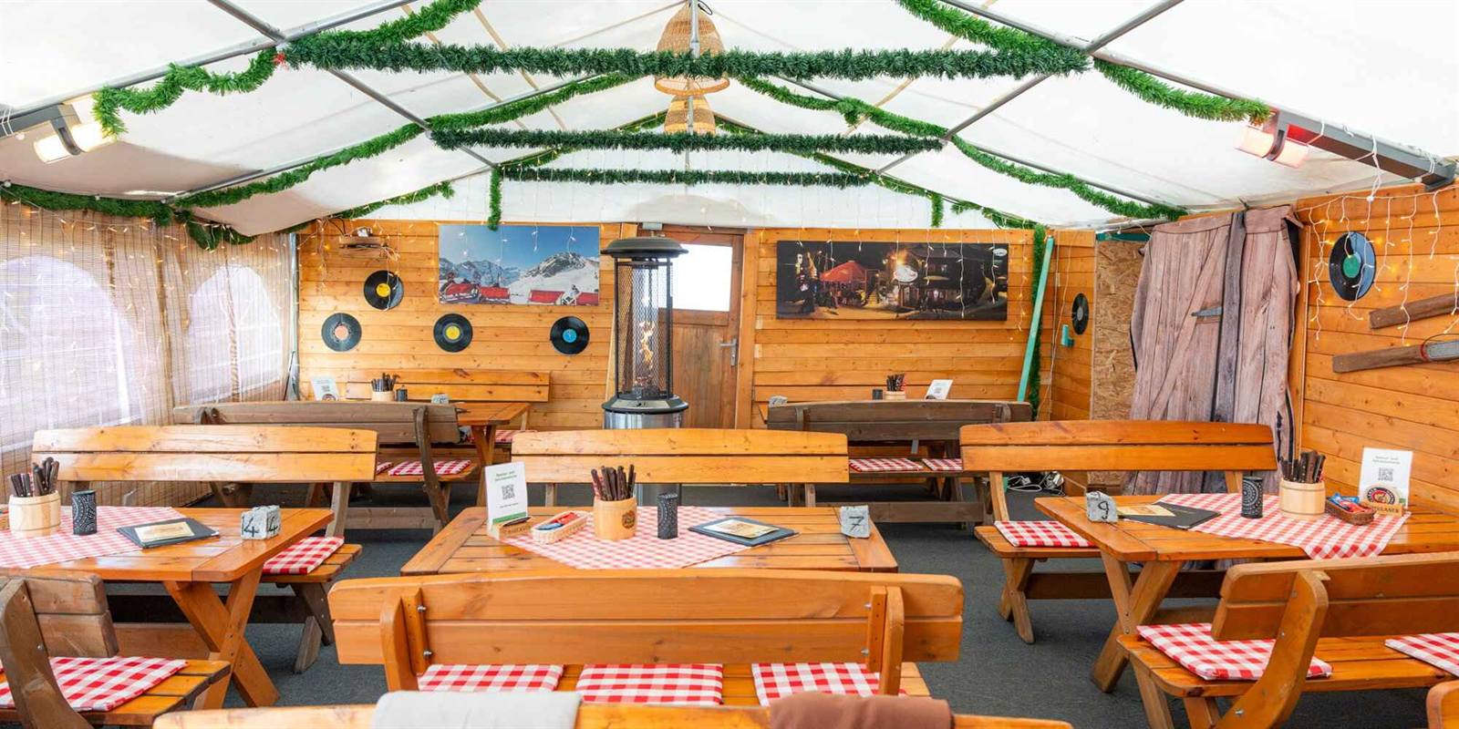Beheiztes Zelt der Schnitzel-Hütte mit langen Holzbänken und rot-weiß karierten Decken